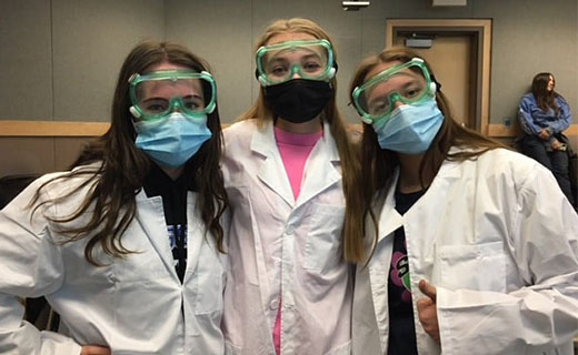 three students in white lab coats and goggles